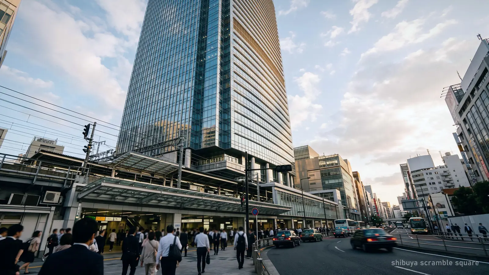 A tall glass tower rising directly above a busy Tokyo railway station, seen from street level