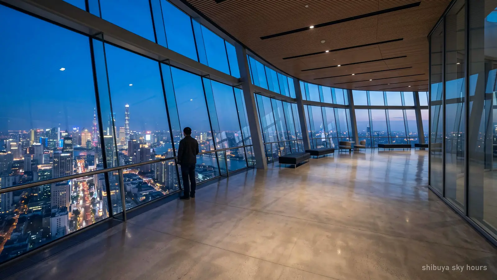 An almost empty observation deck interior in the late evening, the lit city outside