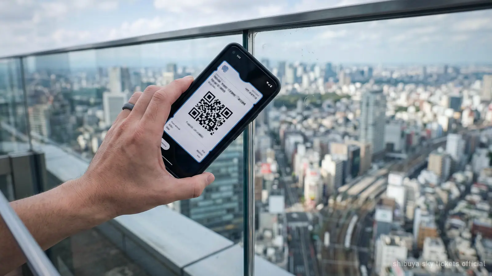 A phone held at the glass edge of a high observation deck, the city blurred far below